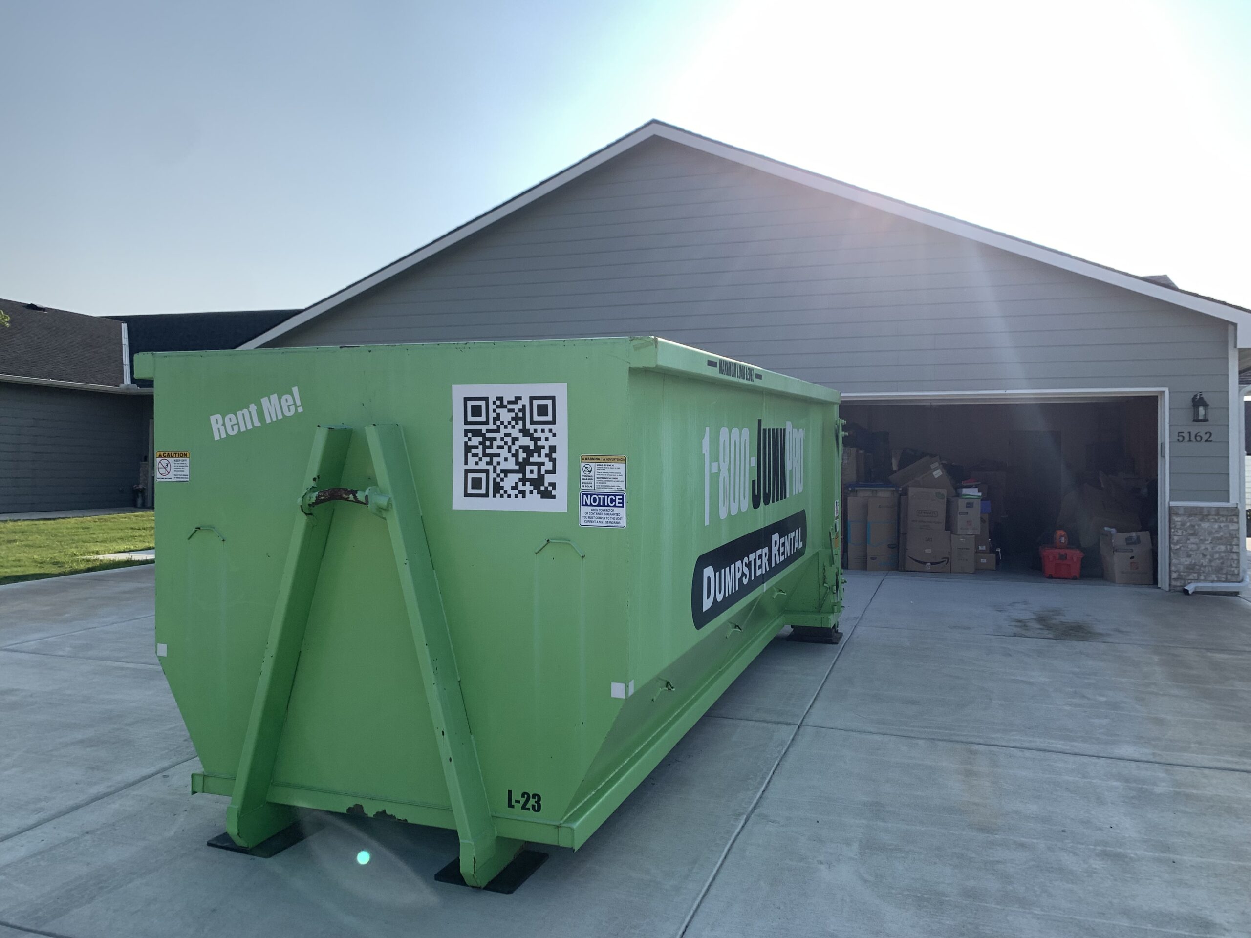 A Large Rented Dumpster in a Residential Driveway with a garage full of junk